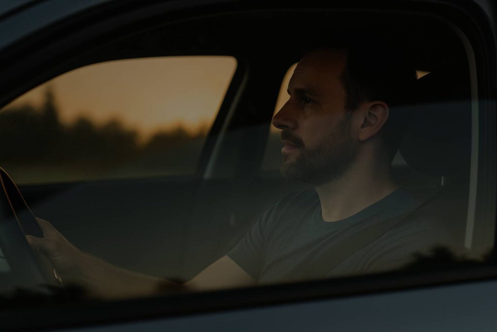 Driver in a car with dark tinted windows, highlighting how window tinting reduces glare and heat for safer driving.