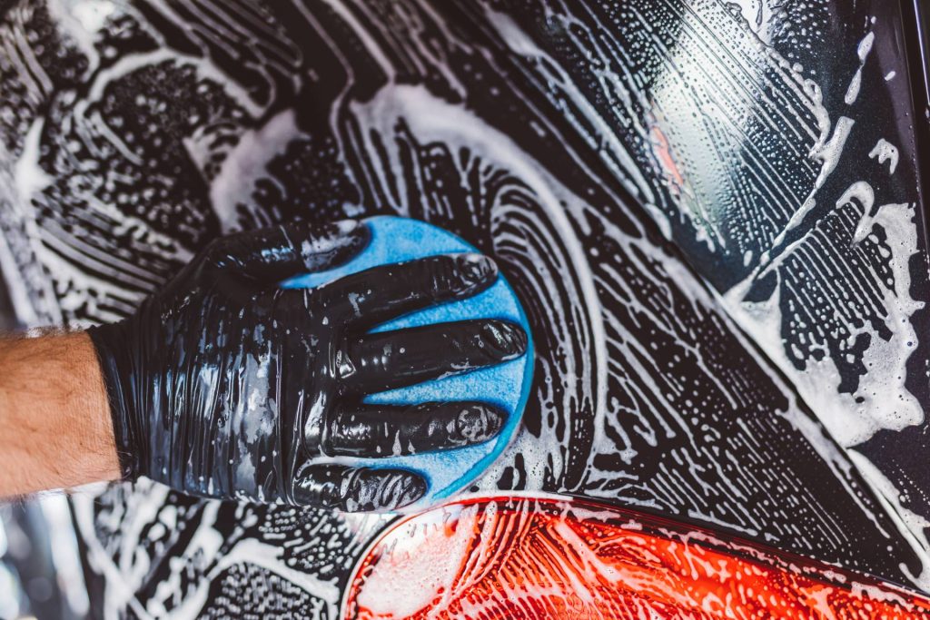 Professional hand car wash using a foam sponge to gently clean and protect car paint surface.